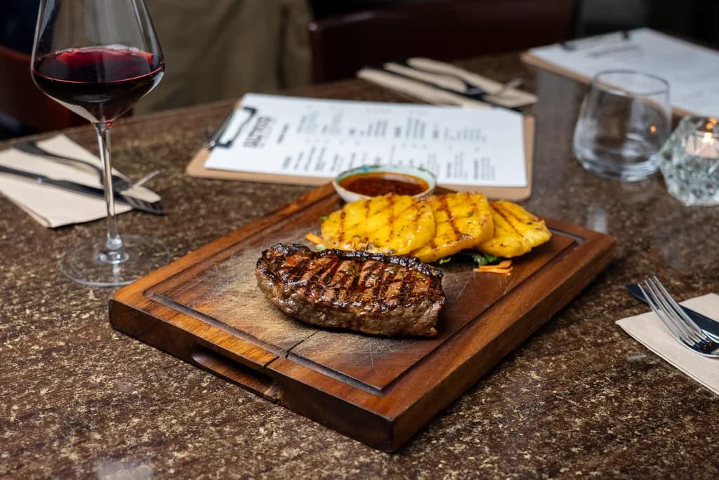 Glass of red wine alongside a wood-fired ribeye steak at Saltwood, Ferrymead.
